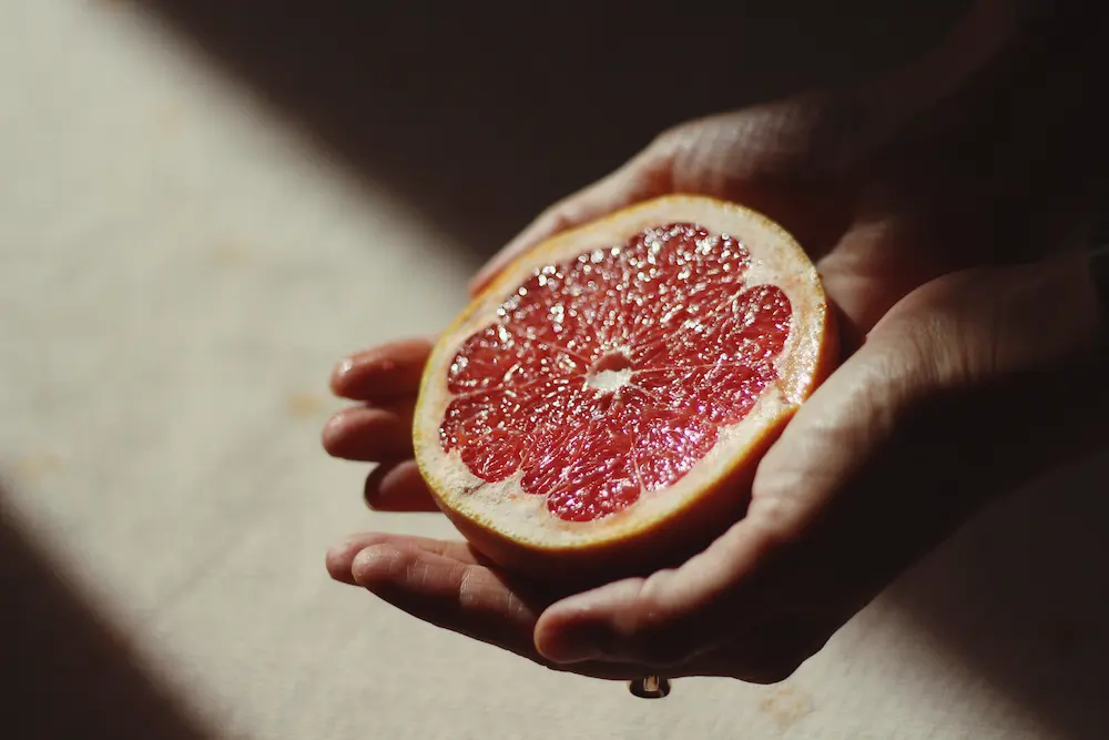 Foco em mãos segurando metade de laranja moro iluminadas por raio de luz